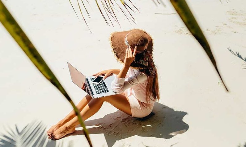 woman working on laptop while sitting on beach